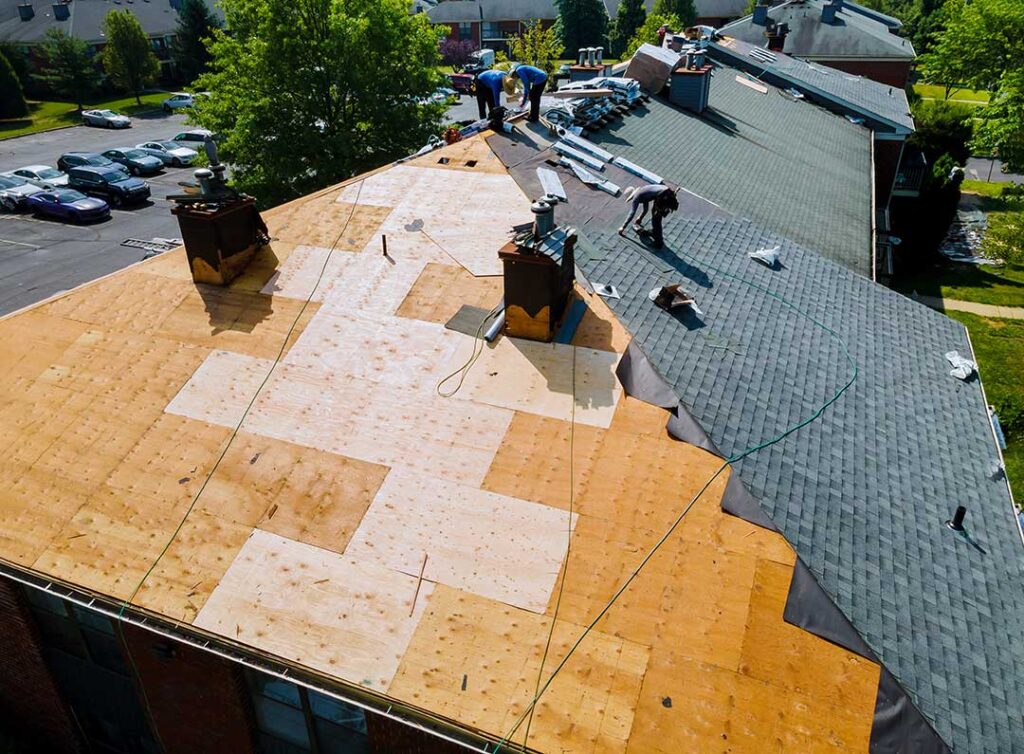 A person carefully placing a tarp over a damaged section of residential roof on a cloudy day.